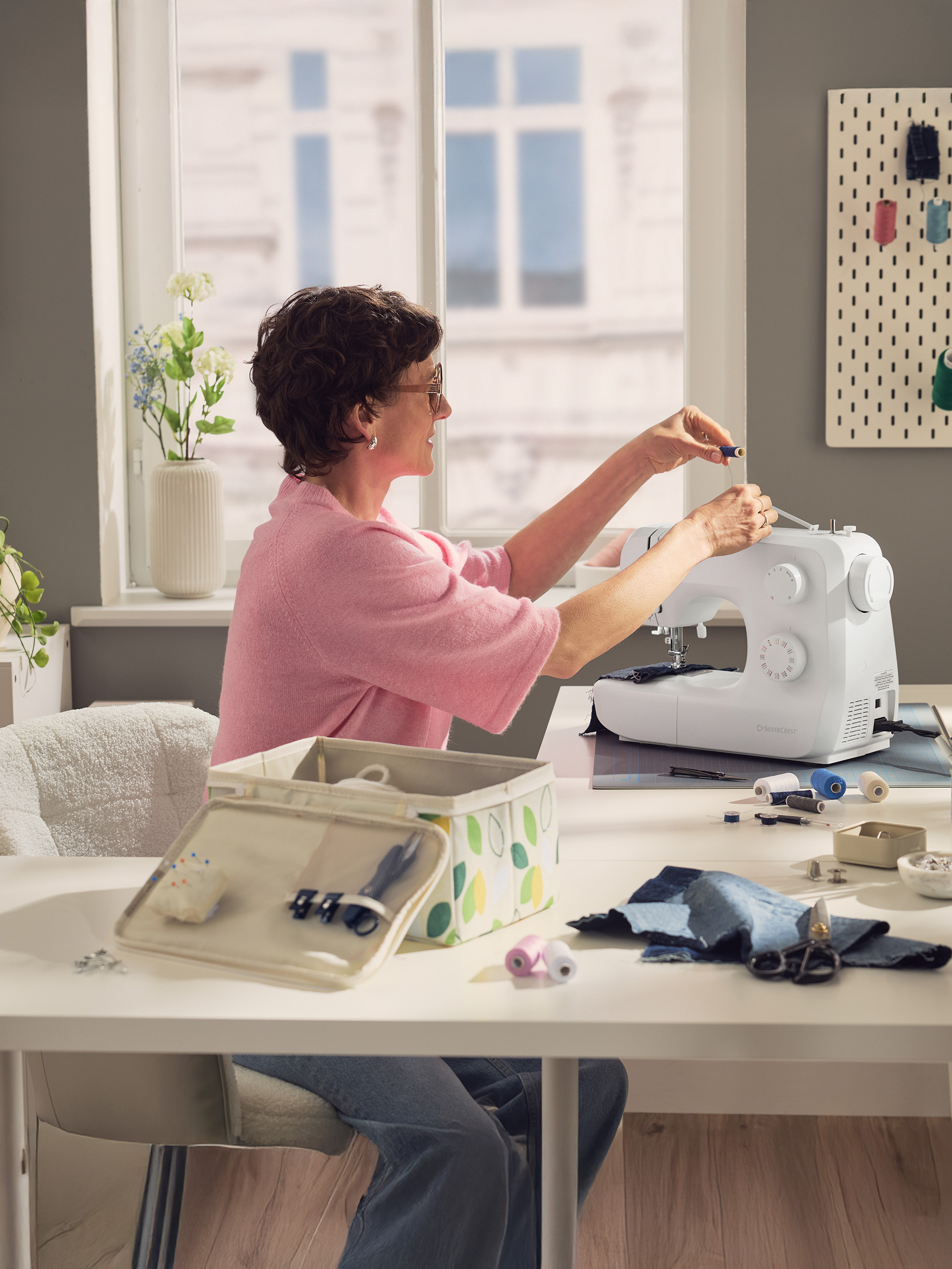 Vrouw naait op naaimachine, met naaibenodigdheden op tafel.