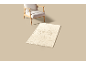 Beige fauteuil en een rechthoekig vloerkleed met rozenpatroon op een lichte achtergrond.