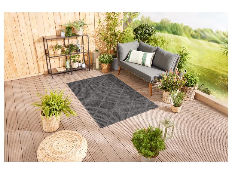 Een grijs tapijt met ruitmotief op een houten terras met planten en een bank.