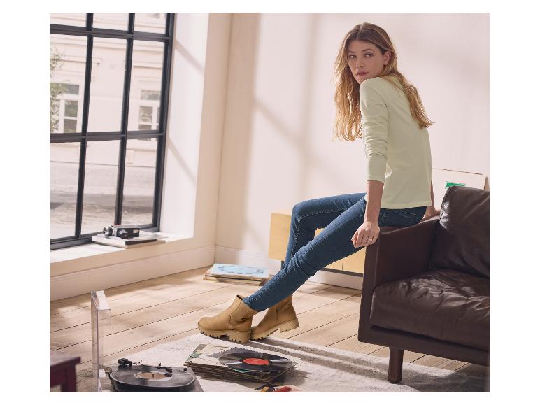 Vrouw in lichtgroen trui en jeans zit op een leren bank, met beige enkellaarsjes aan.