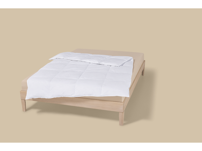 Een bed met een wit dekbed en een lichtbeige hoeslaken.