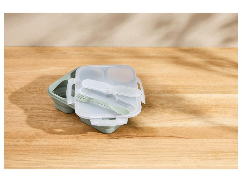 Groene opvouwbare lunchbox met bestek op een houten tafel.