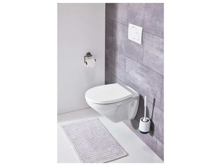 Een witte toiletpot met een geïntegreerde toiletbril, een toiletborstel en een badmat.