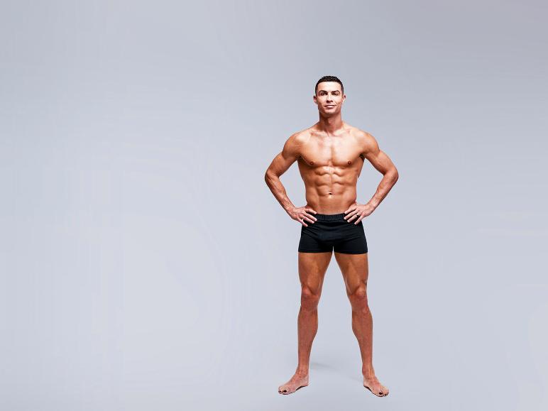 Shirtloze man in zwarte boxershort met handen in de zij, staand tegen een lichtgrijze achtergrond.