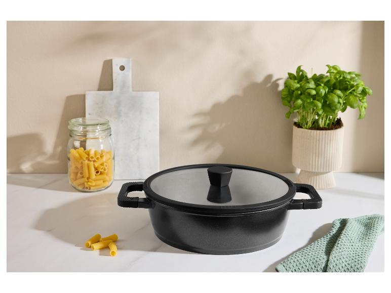 Zwarte pan met deksel, pasta in een glazen pot en basilicum op een aanrecht.