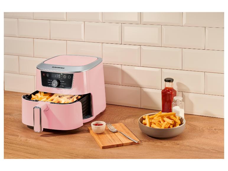 Roze airfryer met friet, ketchup en zout op een houten aanrecht.