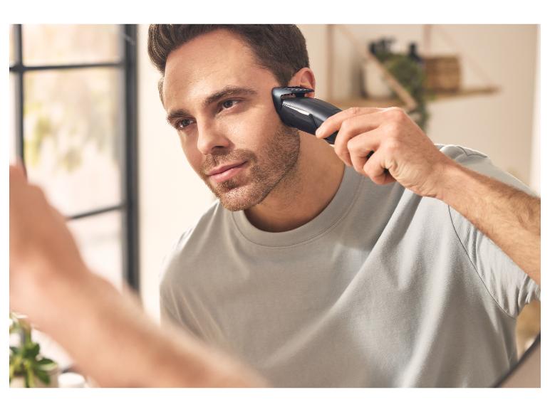 Man scheert zich met een elektrische trimmer, kijkend in de spiegel.