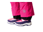 Roze kinder sneeuwbroek met sneeuwvlokembleem en paarse en roze winterlaarzen.