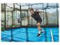 Padelspeler op de baan, gekleed in zwarte sportkleding, slaat de bal met een racket.