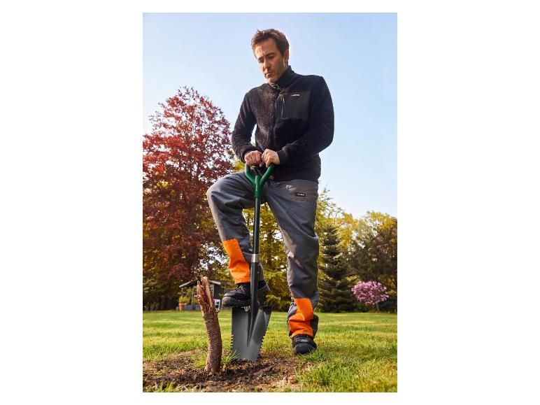 Man in zwart fleecejack en oranje-grijze werkbroek met schop in de tuin.