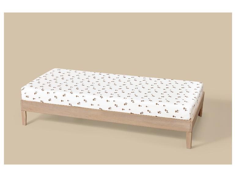 Verschoonkussen met witte hoes met bruin paddenstoelenpatroon, op een houten frame.