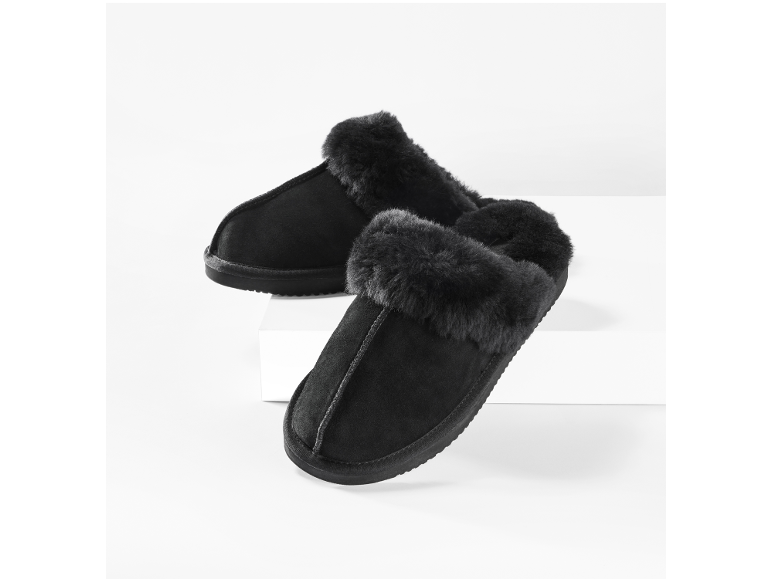 Zwarte suède pantoffels met bontvoering op een witte achtergrond.