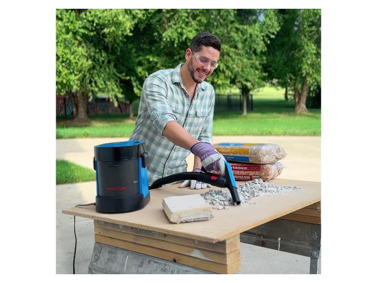 Man gebruikt een Invictus stofzuiger om puin op te ruimen op een buitenwerkbank.