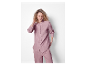 Een vrouw in een lichtroze pyjama met een shirt met lange mouwen en broek.