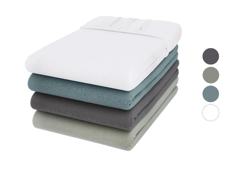 Stapel hoeslakens in diverse kleuren: wit, blauw, donkergrijs en lichtgroen.