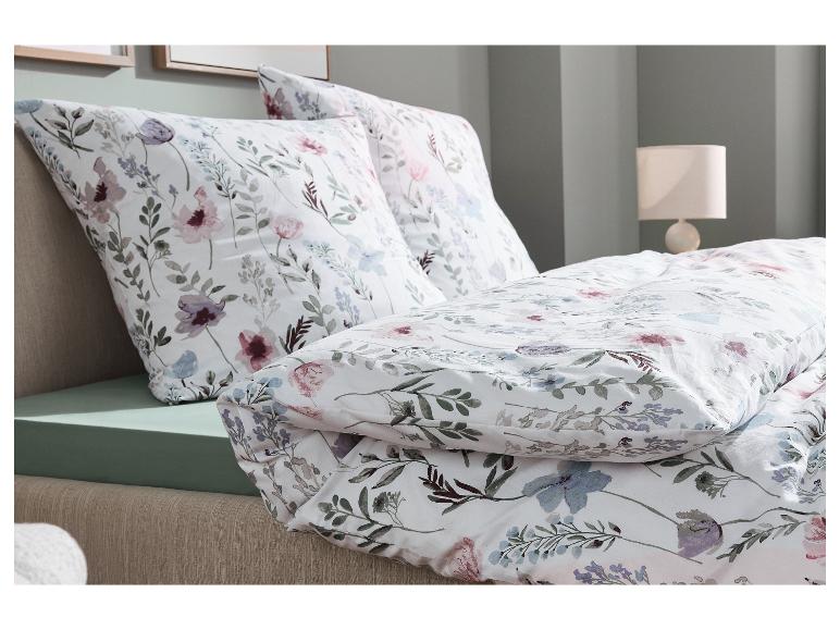 Bloemig beddengoed in wit, roze en paars op een bed met een groen hoeslaken.
