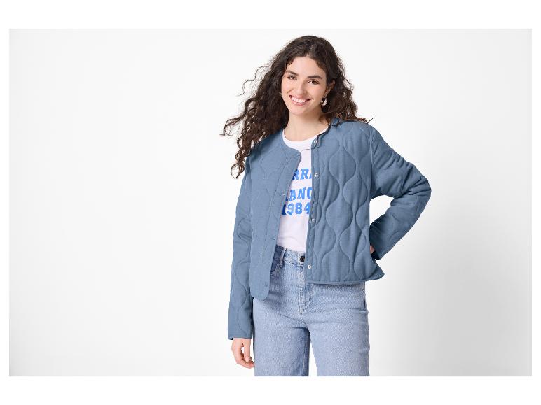 Vrouw in blauw gewatteerd jack, wit T-shirt met tekst en jeans.