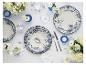 Wit en blauw servies met bloemmotieven, bestek en bloemstukken op een witte tafel.