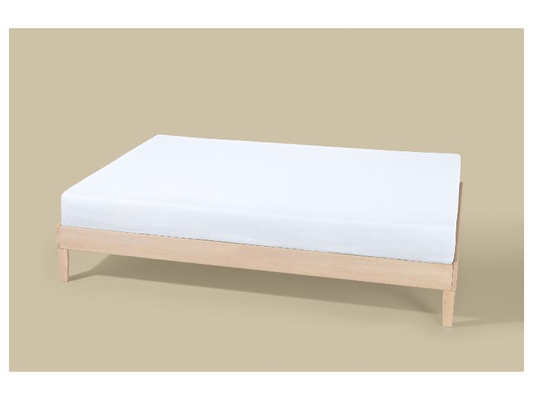 Een wit matras op een licht houten bedframe tegen een beige achtergrond.