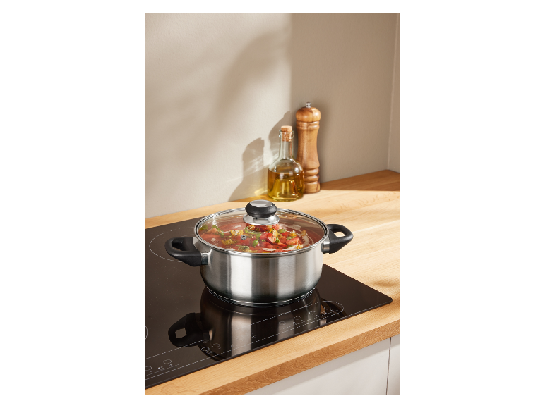 Een roestvrijstalen pan met deksel kookt soep op een inductiekookplaat.