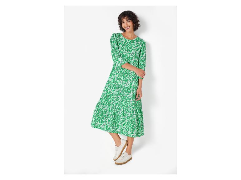 Een vrouw in een groene gebloemde jurk en witte sneakers.