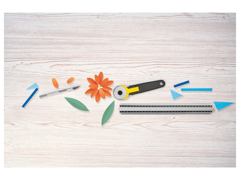 Een snijmat, een rolmes en een papieren bloem op een houten tafel.