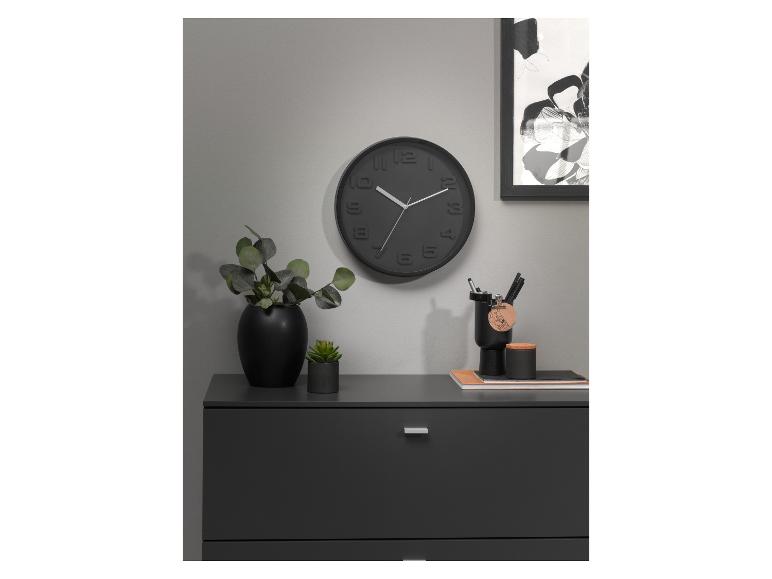 Zwarte wandklok, vaas, planten en bureauaccessoires op een donkergrijs meubel.