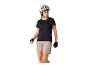 Vrouw in zwart fietsshirt, beige korte broek en witte helm, kijkt naar rechts.
