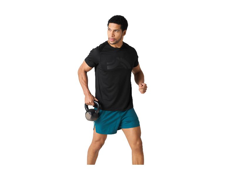 Een man in een zwart shirt en teal shorts houdt een kettlebell vast.