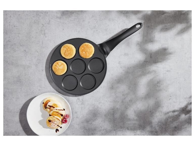 Pan met pannenkoeken en een bord met versierde pannenkoeken op een betonnen ondergrond.