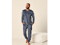 Man in donkerblauwe velours pyjama, lachend en staand naast een witte poef.