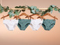 Vier paar onderbroeken, twee wit en twee groen met witte stippen, hangen aan houten hangers.