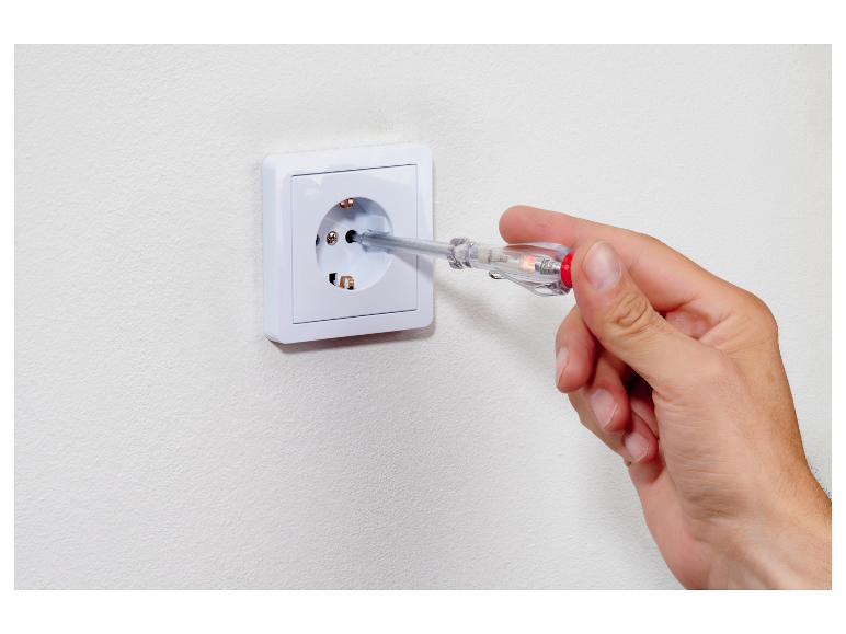 Hand houdt spanningszoeker in stopcontact.