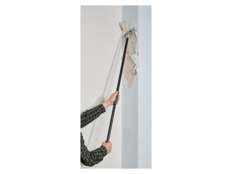 Een man gebruikt een gereedschap om behang van een muur te verwijderen.