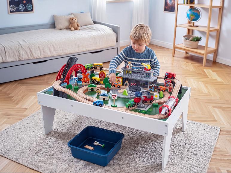 Jongen speelt met houten treintafel met bruggen en gebouwen in kinderkamer.