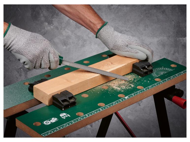 Man vijlt een houten plank vastgeklemd op een werkbank.