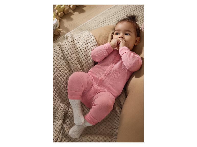 Baby in een roze romper ligt op een gebreide deken, met houten speelgoed op de achtergrond.