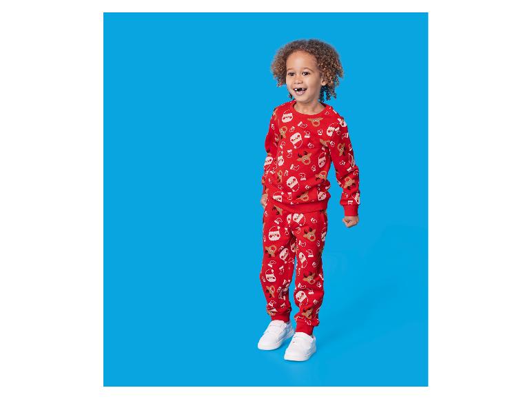 Kind in een rode kerstpyjama met print, op een blauwe achtergrond.