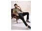 Man in een beige T-shirt en zwarte broek zit in een fauteuil.