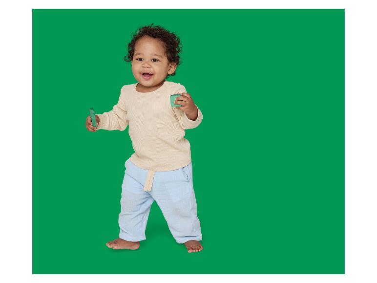Lachende baby in beige en blauwe pyjama, met groene bouwblokken.