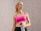 Een vrouw in een roze sportbeha en zwarte leggings houdt een waterfles vast.
