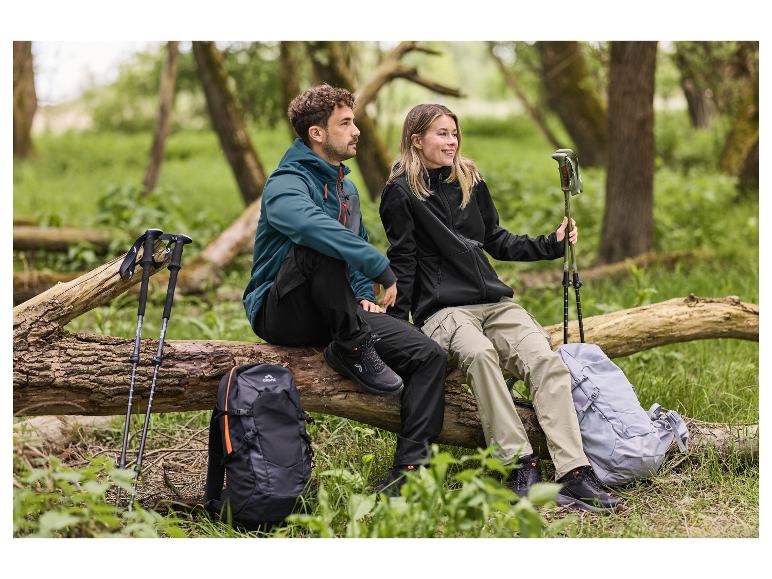 Twee wandelaars in wandeljassen en -broeken, zittend op een boomstam met rugzakken en wandelstokken.