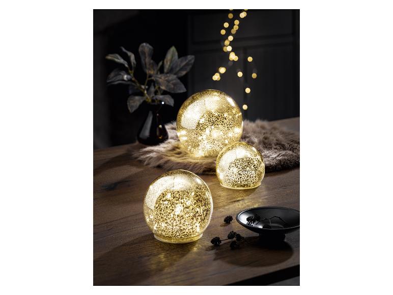 Drie gouden lichtgevende bollen op een houten tafel, met herfstdecoraties.