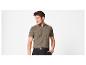 Man in een bruin gebreid poloshirt en zwarte broek, poserend met hand in zak.