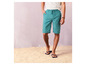 Man in groene shorts en slippers op het strand.
