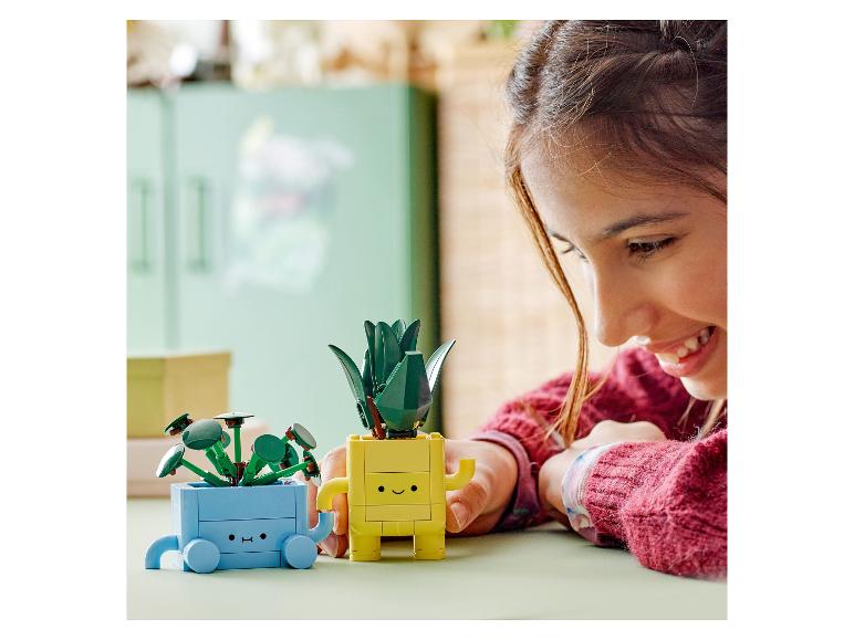 Een meisje lacht terwijl ze met twee LEGO Botanicals planten op een tafel speelt.
