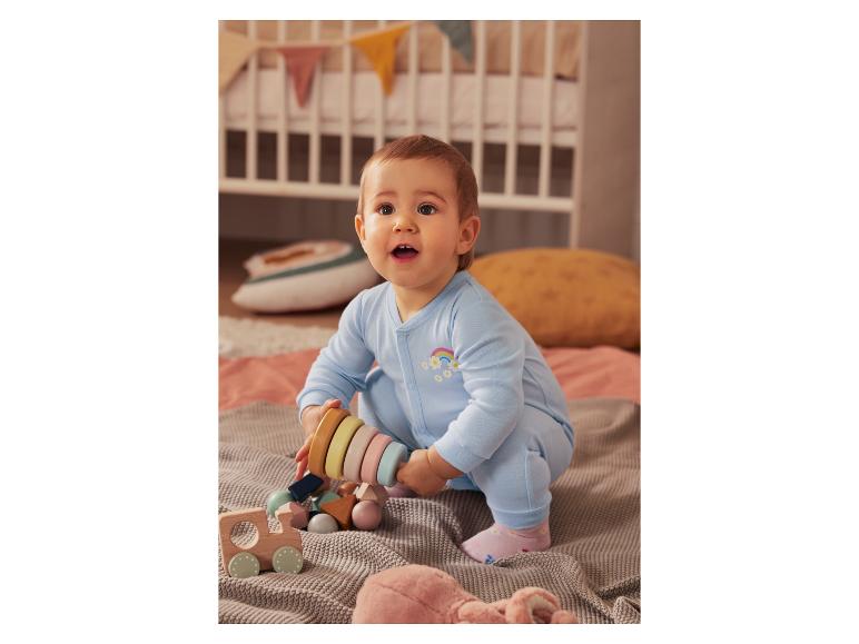 Een baby in een blauwe romper speelt met houten speelgoed.