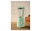Mintgroene blender op een aanrecht, met lichte tegels en houten snijplanken op de achtergrond.