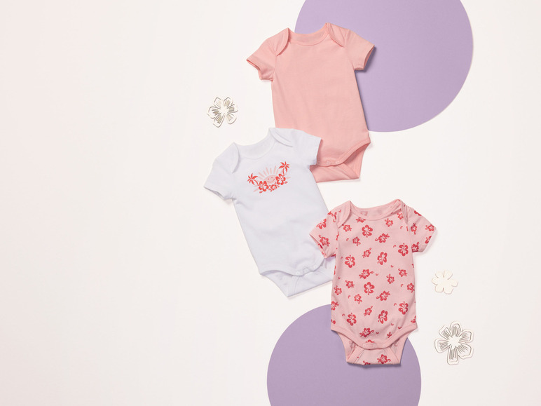 Drie baby-onesies met korte mouwen: roze effen, wit met palmen en roze met bloemen.