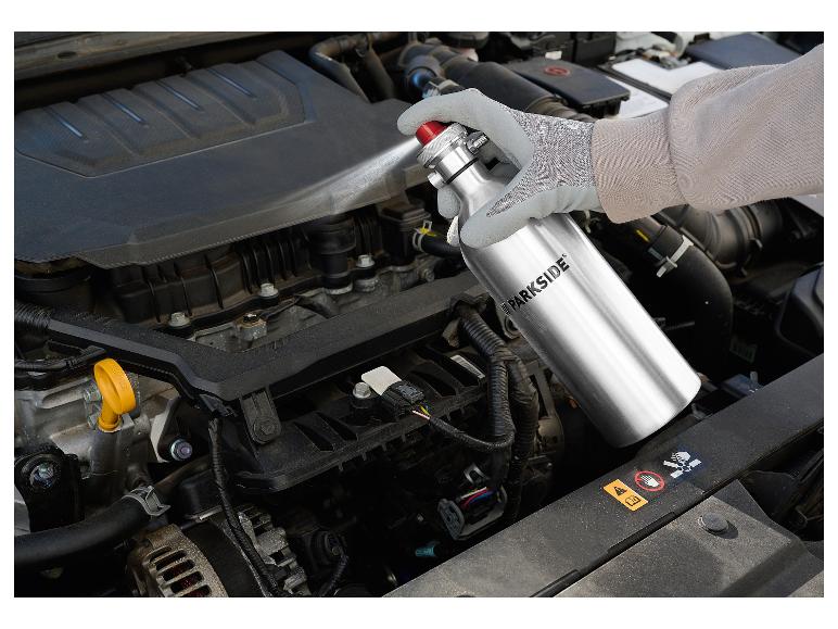 Gehandschoende hand spuit reiniger op een automotor.